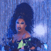 a drag queen wearing a black top with stars on it is standing in front of a blue curtain
