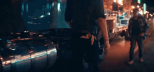 two men are walking down a street at night and one has a gun in his belt