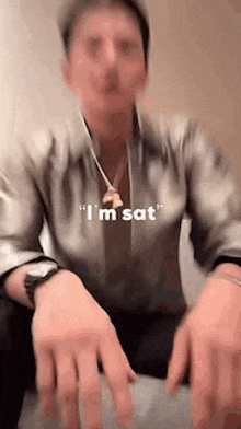 a man wearing a watch and a necklace says i 'm sat while sitting on a chair .