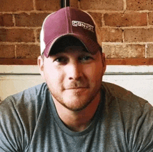 a man wearing a hat and a grey shirt is sitting in front of a brick wall .