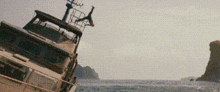 a boat is floating on its side in the ocean with a large rock in the background .