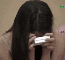 a woman covering her face while holding a box in front of a sign that says kao