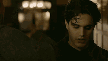a man with curly hair is standing in a dark room and looking down .