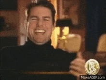 a man in a turtleneck is laughing and clapping his hands .