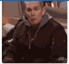 a man in a bomber jacket is sitting on a couch smoking a cigarette .