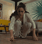a woman is squatting on the floor in a living room with a couch in the background