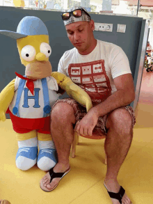 a man is sitting next to a stuffed homer simpson with the letter h on his shirt