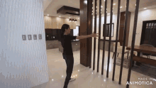 a woman in a black shirt is standing in a room with a wooden divider between the kitchen and dining room .
