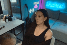 a woman is sitting in front of a neon sign that says khaleesi