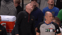a man in a black nike jacket stands next to a referee during a basketball game