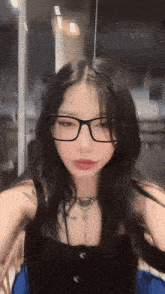 a girl wearing glasses and a black tank top is sitting in a chair .
