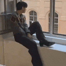 a man is sitting on a window sill with his legs crossed and looking out the window .