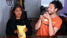 a man is taking a picture of a woman holding a bag of corn chips