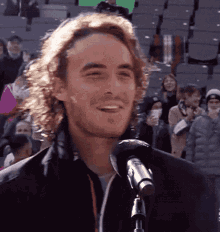 a man with curly hair is smiling while talking into a microphone