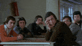 a group of men are sitting at a table with their hands on their faces