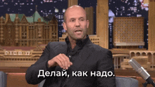 a man in a suit is sitting in front of a microphone with the words " делай как надо " written below him