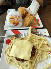 a plate of spaghetti and french fries next to a burger
