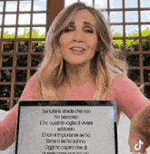 a woman in a pink shirt is holding a laptop that says " sei tutte le strade che non ho percorso " on the screen