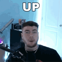 a man with a beard is standing in front of a microphone with the word up written above him .