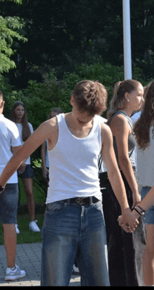 a man in a white tank top is standing in a circle of people holding hands