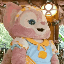 a stuffed animal wearing overalls and a yellow collar is standing next to a lamp .