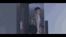 a man in a plaid shirt is standing in a doorway with a black bag .