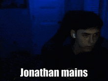 a man is sitting in front of a computer screen in a dark room with the words `` jonathan mains '' written on the screen .