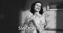 a woman is standing in a room with her hands on her chest and the word swooning written on the screen .