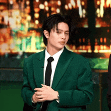 a man in a green suit and black tie is standing with his hands folded