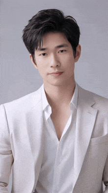 a young man in a white suit and white shirt is looking at the camera