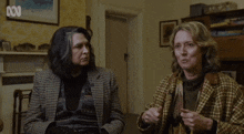 two women are sitting in a room with a picture on the wall above them that says abc