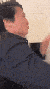 a man in a blue jacket is making a funny face while standing in front of a wall .