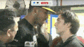 a man in a yellow hat is talking to another man in a black shirt .