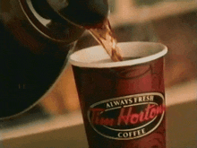 a cup of tim hortons coffee is being poured from a kettle