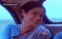 a woman in a blue shirt is sitting in the back seat of a car and smiling .