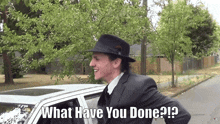 a man in a suit and hat is standing in front of a car with the words " what have you done " on the bottom