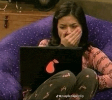 a woman is sitting on a purple bean bag chair using a laptop computer .