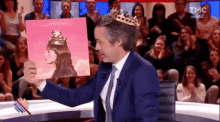 a man in a suit and tie is wearing a crown and holding a pink album cover .