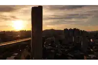 a sunset over a city with a very tall building in the foreground that says ' samsung ' on it
