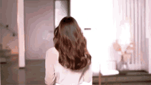 a woman with long brown hair is standing in a living room looking at the camera .