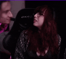 a woman with red hair and glasses is sitting in a racing chair .