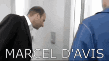 a man in a suit is talking to a man in a blue jacket with the name marcel d' avis written on the bottom