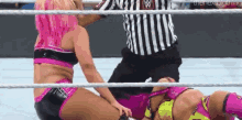 two women are wrestling in a ring and a referee is standing behind them .