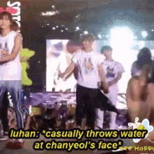 a group of people are standing on a stage and one of them says luhan casually throws water at chanyeol 's face