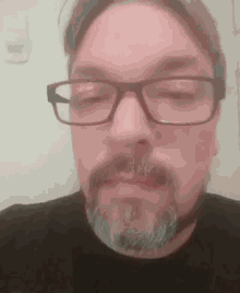 a man with glasses and a beard is wearing a black shirt .