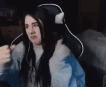 a woman is sitting in a gaming chair wearing headphones and looking at the camera .