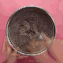 a person is mixing something in a metal bowl on a pink surface .