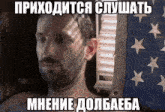 a man with a beard is laying in front of an american flag with russian writing