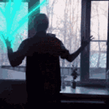 a silhouette of a man standing in front of a window with a green light behind him