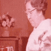 a woman wearing glasses is sitting in front of a vase of flowers